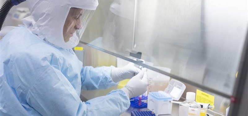 man in PPE using pipette under vent hood
