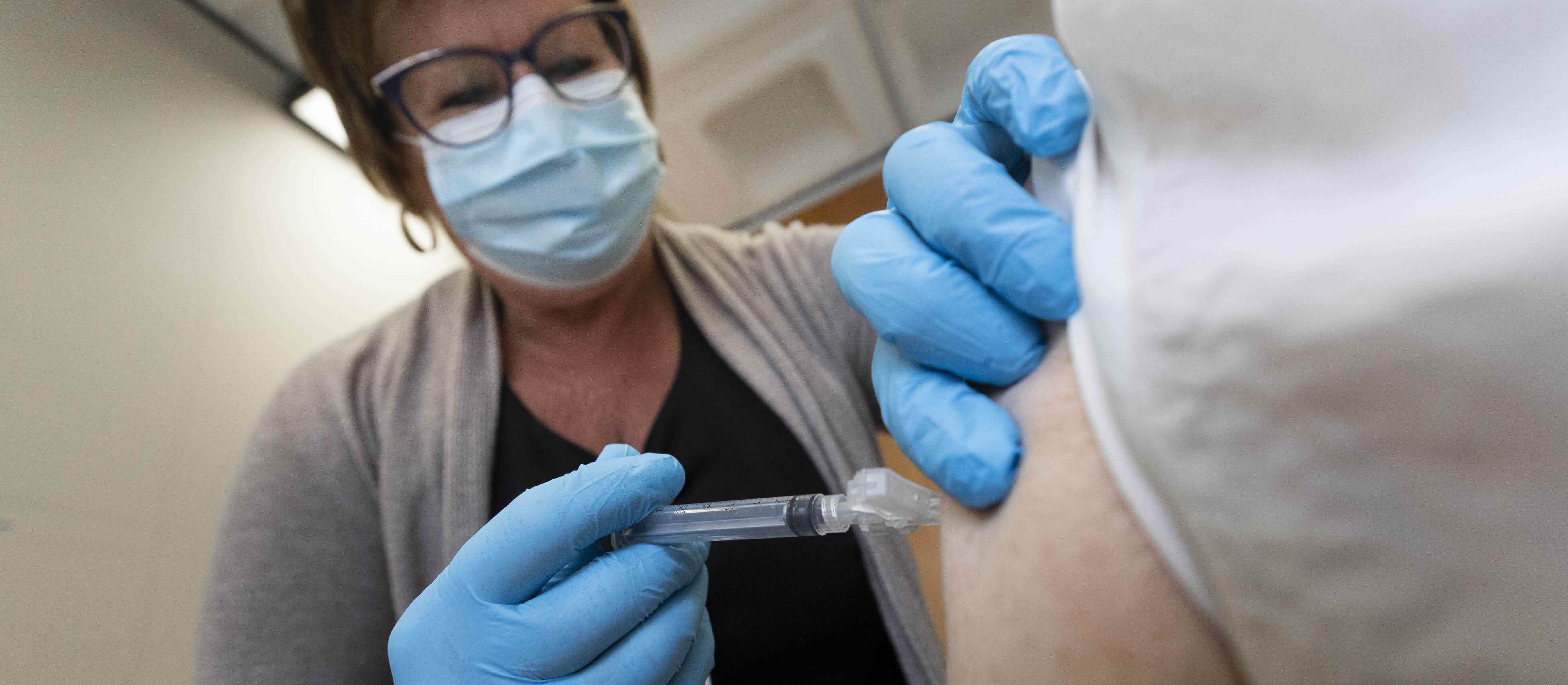 woman wearing PPE face mask putting a needle in a man's arm