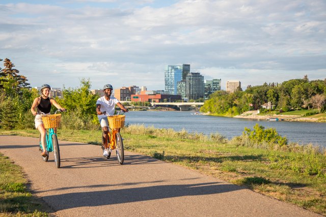 two people riding a bike on a trail alongside a river