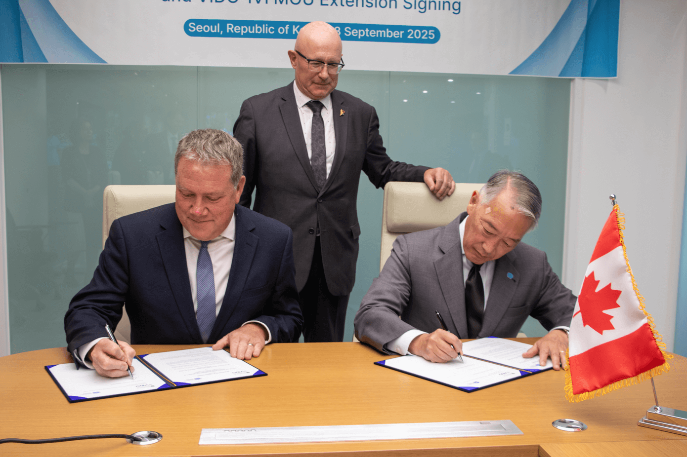 Three individuals at a formal event - two are signing papers